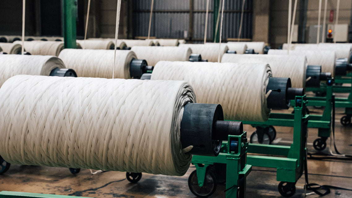 Textile factory with large spools of yarn on green stands.